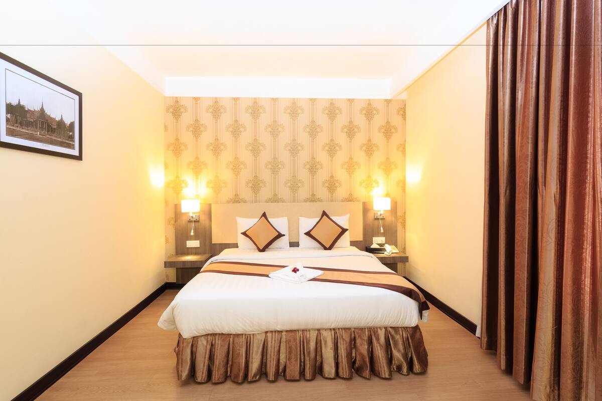 Habitación de hotel con una cama grande, dos lámparas de noche, una mesita de noche y un cuadro en la pared.