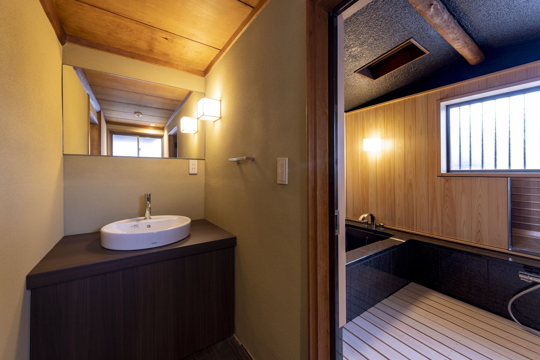 A modern bathroom with a wooden vanity, a round sink, and a mirror. There is a window providing natural light and a view of the outside.