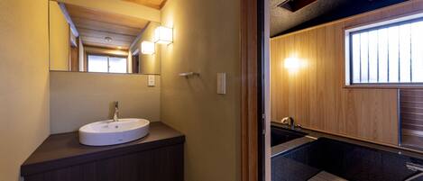 A modern bathroom with a wooden vanity, a round sink, and a mirror. There is a window providing natural light and a view of the outside.