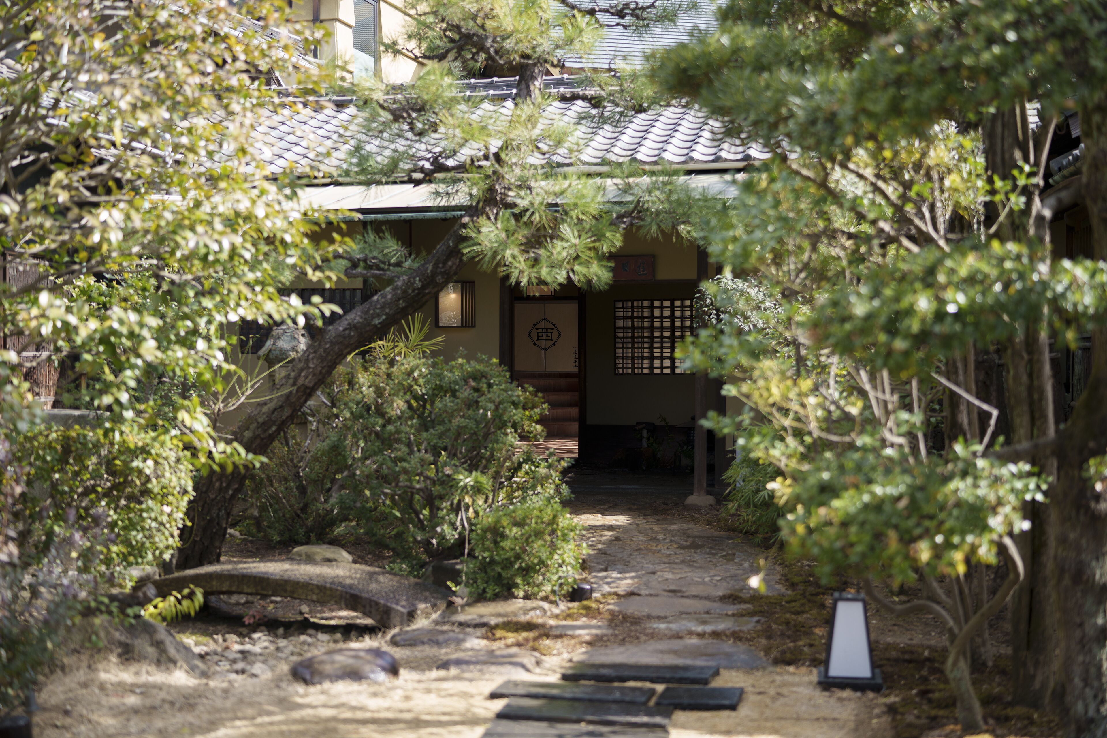 A traditional Japanese garden with a stone pathway leading to a building with a tiled roof.