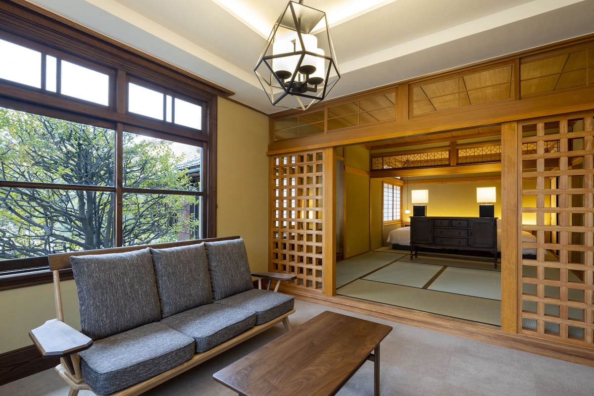 Una habitación japonesa tradicional con suelo de tatami, una mesa de madera baja, un sofá y un divisor de puertas shoji.