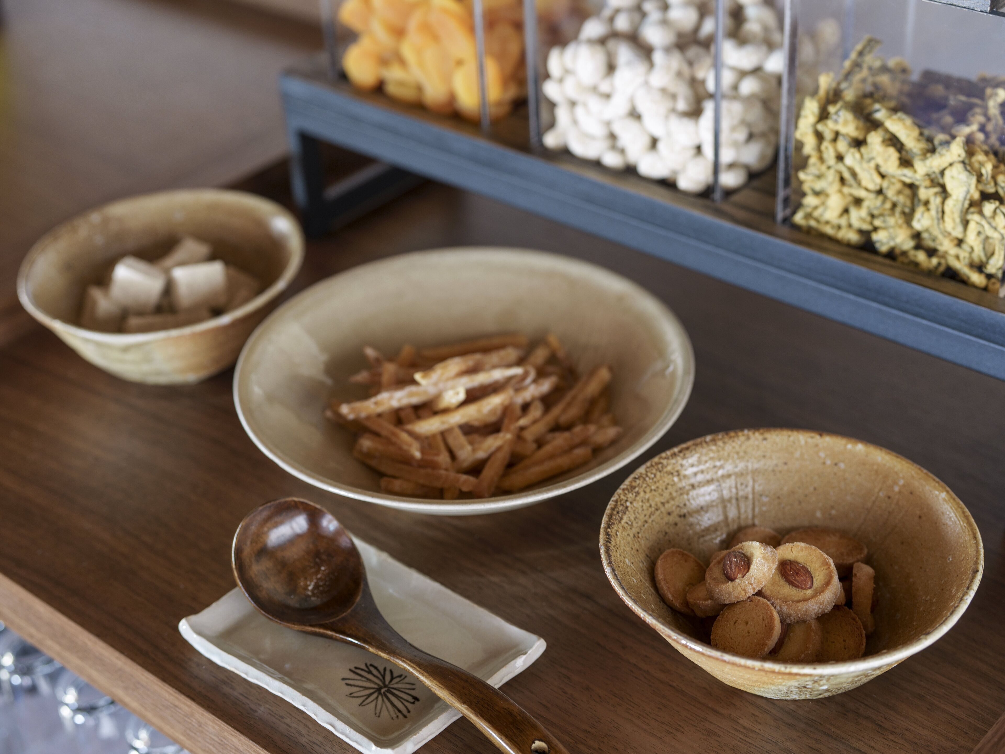 Una mesa de madera con cuencos que contienen diversos alimentos, una cuchara y un plato pequeño.