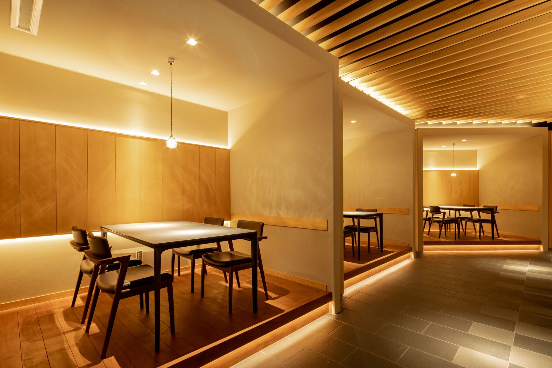 Um interior moderno com paredes de madeira, uma mesa de jantar central e teto inclinado com iluminação embutida.