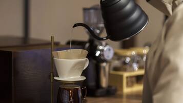 A person pouring liquid from a black kettle into a white cup with a paper filter.