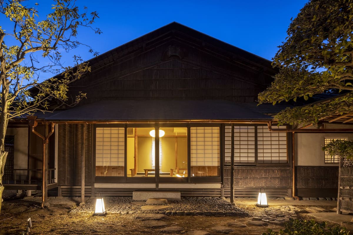 Un edificio japonés tradicional con fachada de madera, amplias puertas correderas y un sendero de piedra que lleva a la entrada.