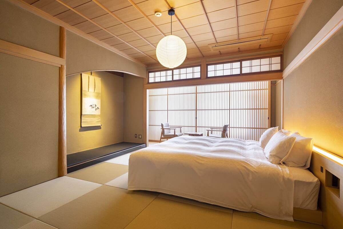 Un dormitorio de estilo japonés tradicional con suelo de tatami, una cama, una puerta corrediza de fusuma y un farolillo de papel colgante.