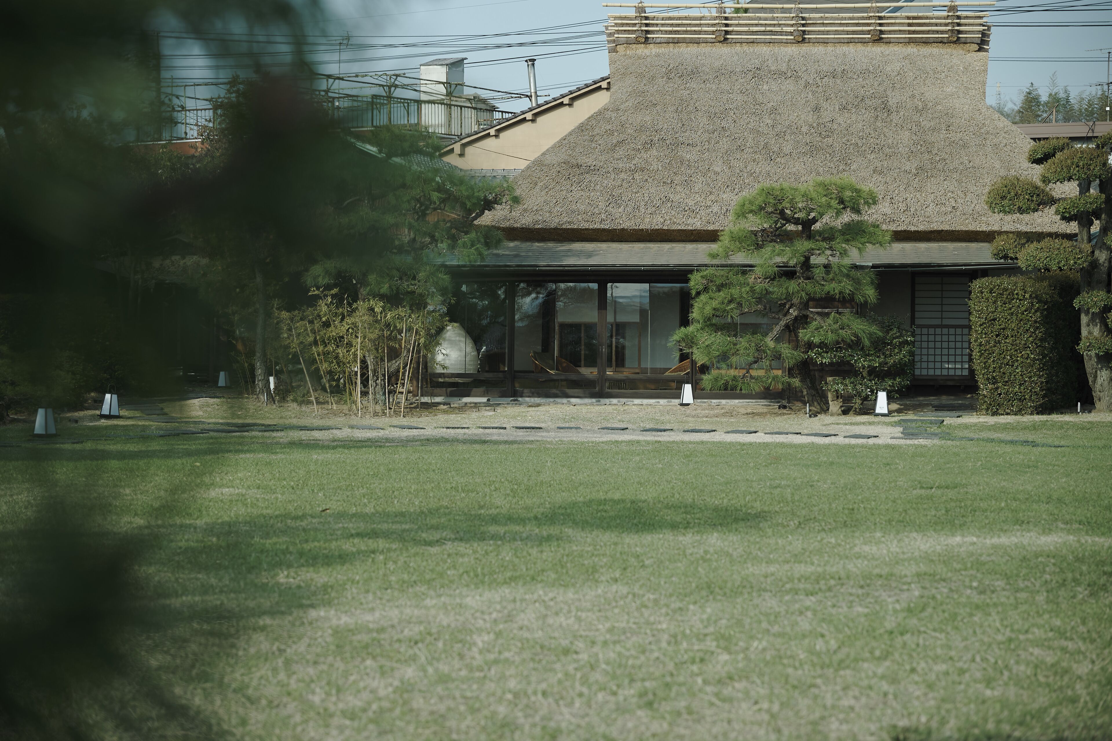 A traditional Japanese building with a thatched roof, surrounded by well-maintained greenery and a clear pathway.