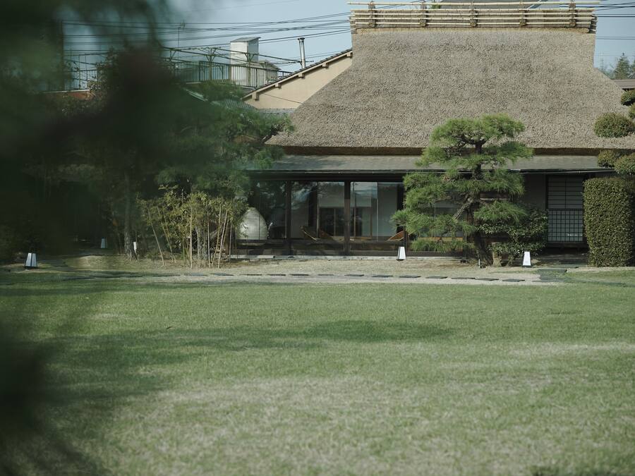A traditional Japanese building with a thatched roof, surrounded by well-maintained greenery and a clear pathway.