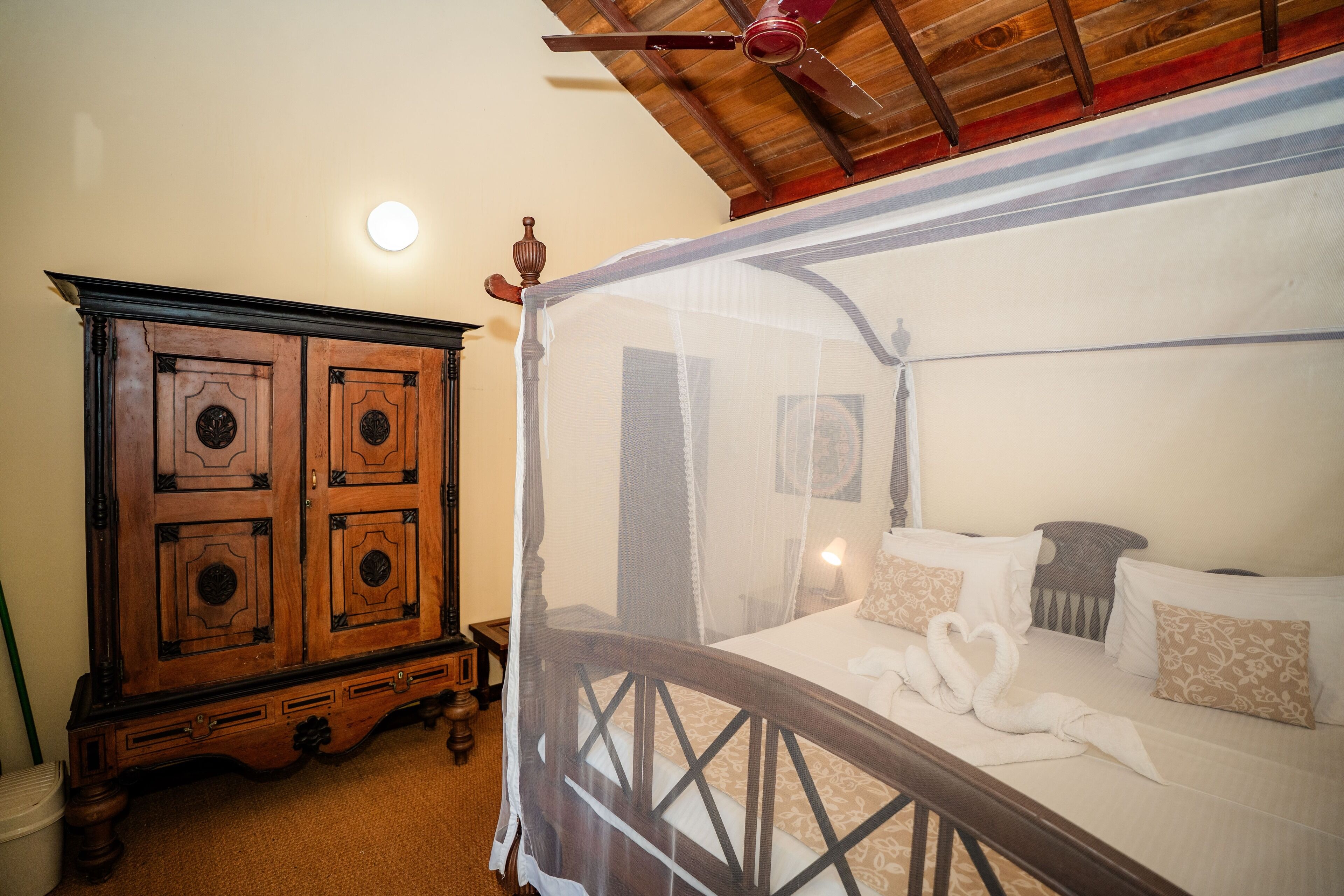 A bedroom with a four-poster bed, a wooden cabinet, and a ceiling fan.