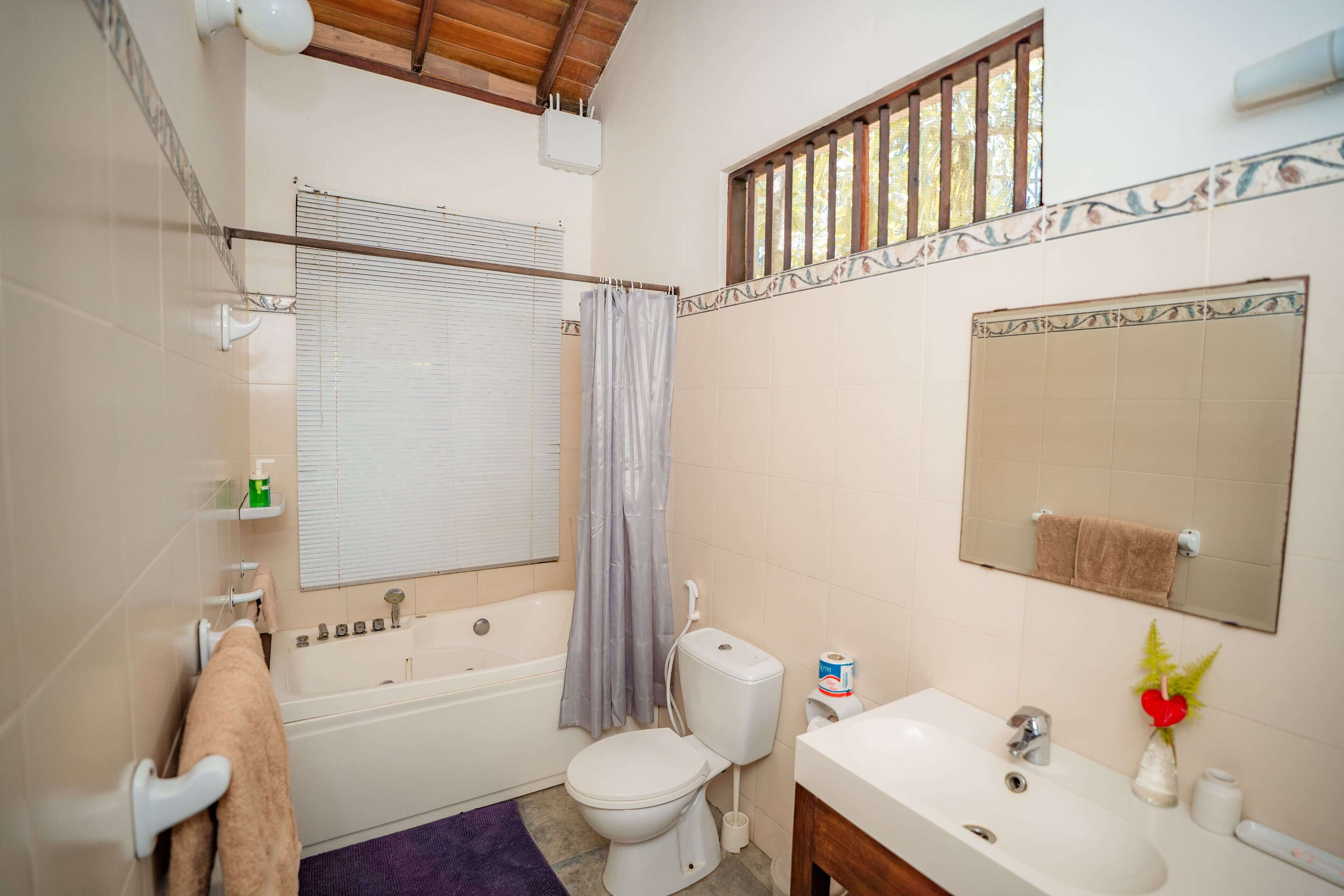 Un baño con bañera, inodoro, lavamanos y ventana con cortina de ducha.