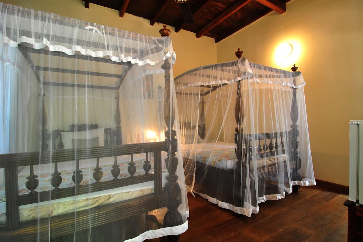 Dos camas con dosel de madera y mosquiteros blancos, cabeceros de madera y suelo de madera.
