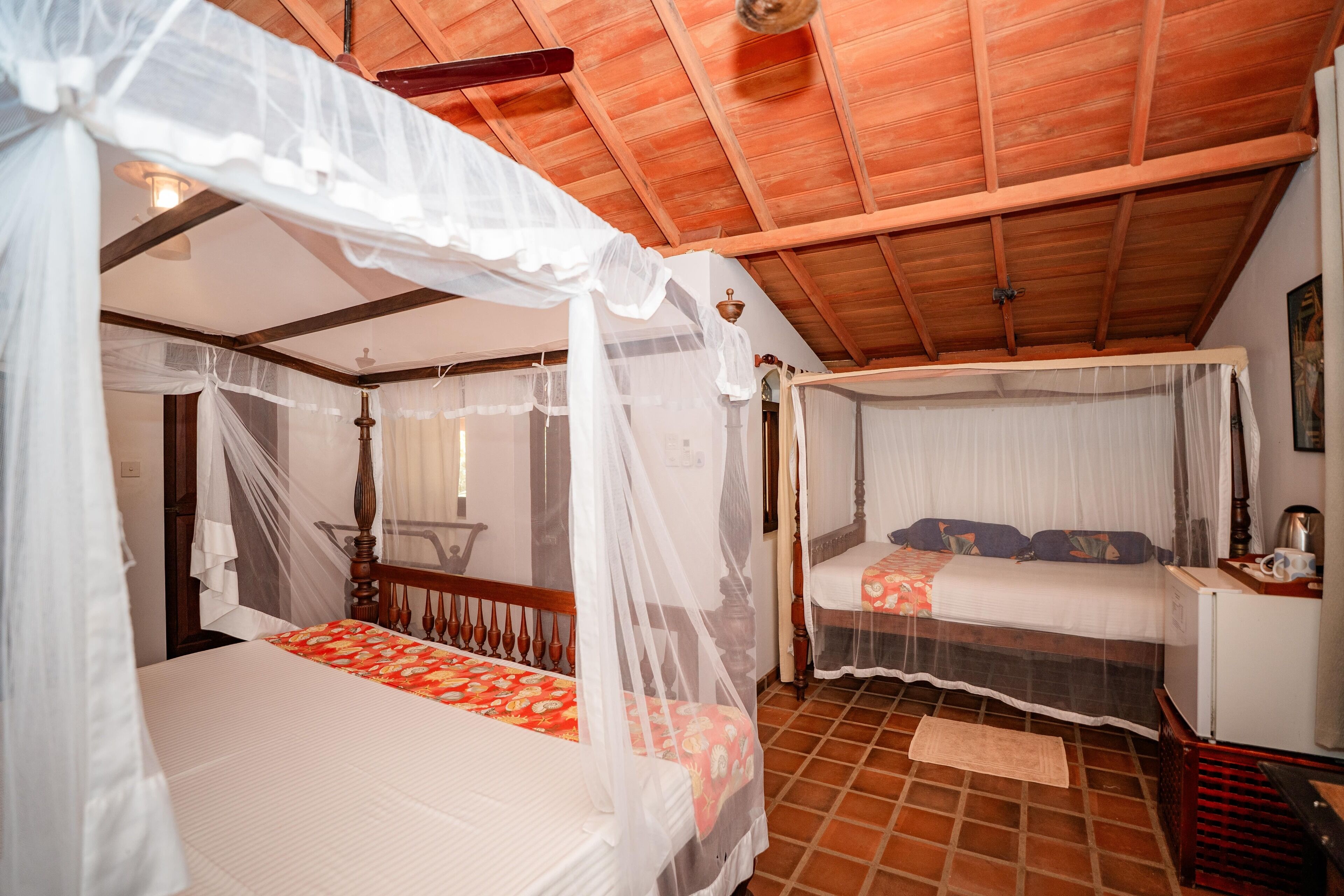 A room with two beds, each with a canopy. The room has wooden ceilings and tiled floors.