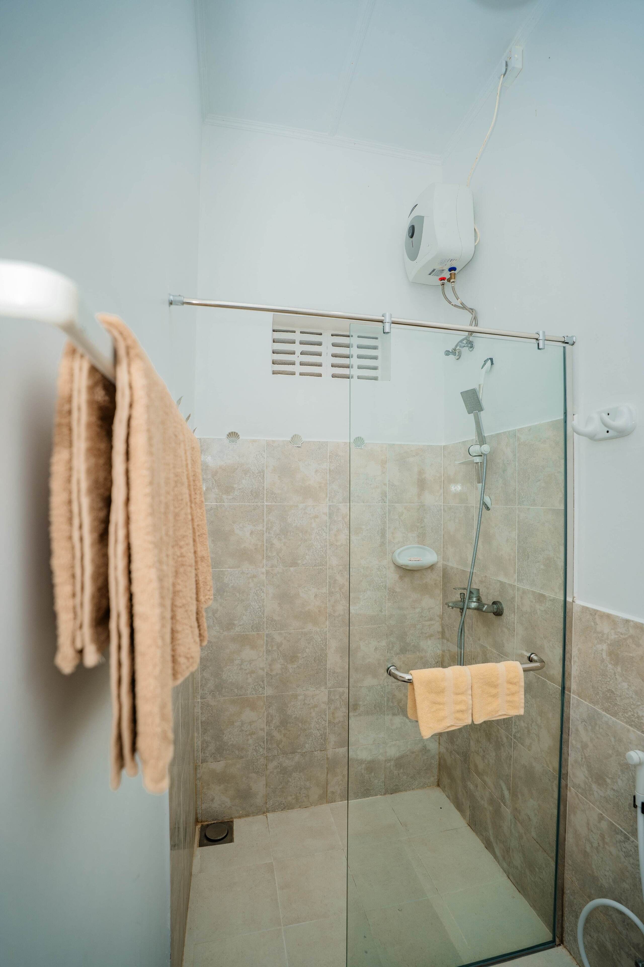 A glass-enclosed shower with a handheld showerhead, a towel rack with two towels, and a soap dispenser on the wall.
