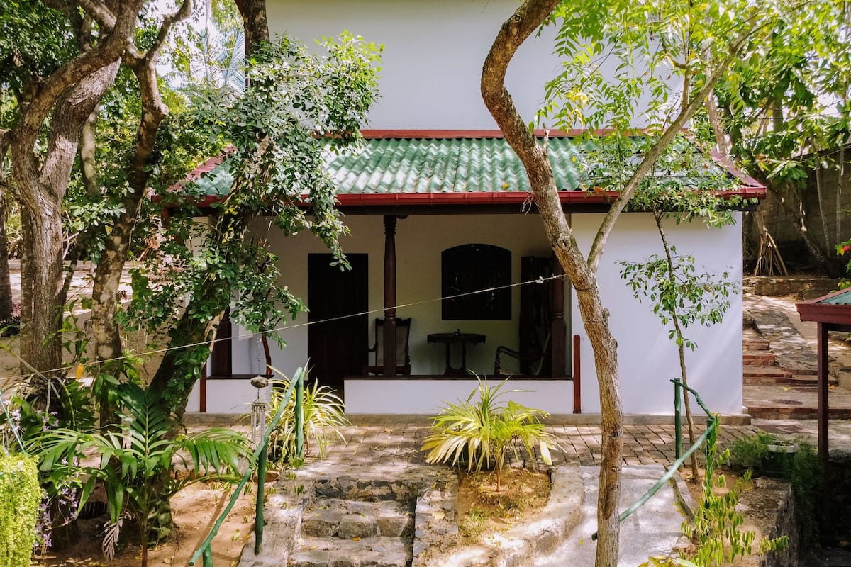Una casa tradicional con techo de tejas, rodeada de exuberante vegetación y una escalera de piedra que conduce a la entrada.