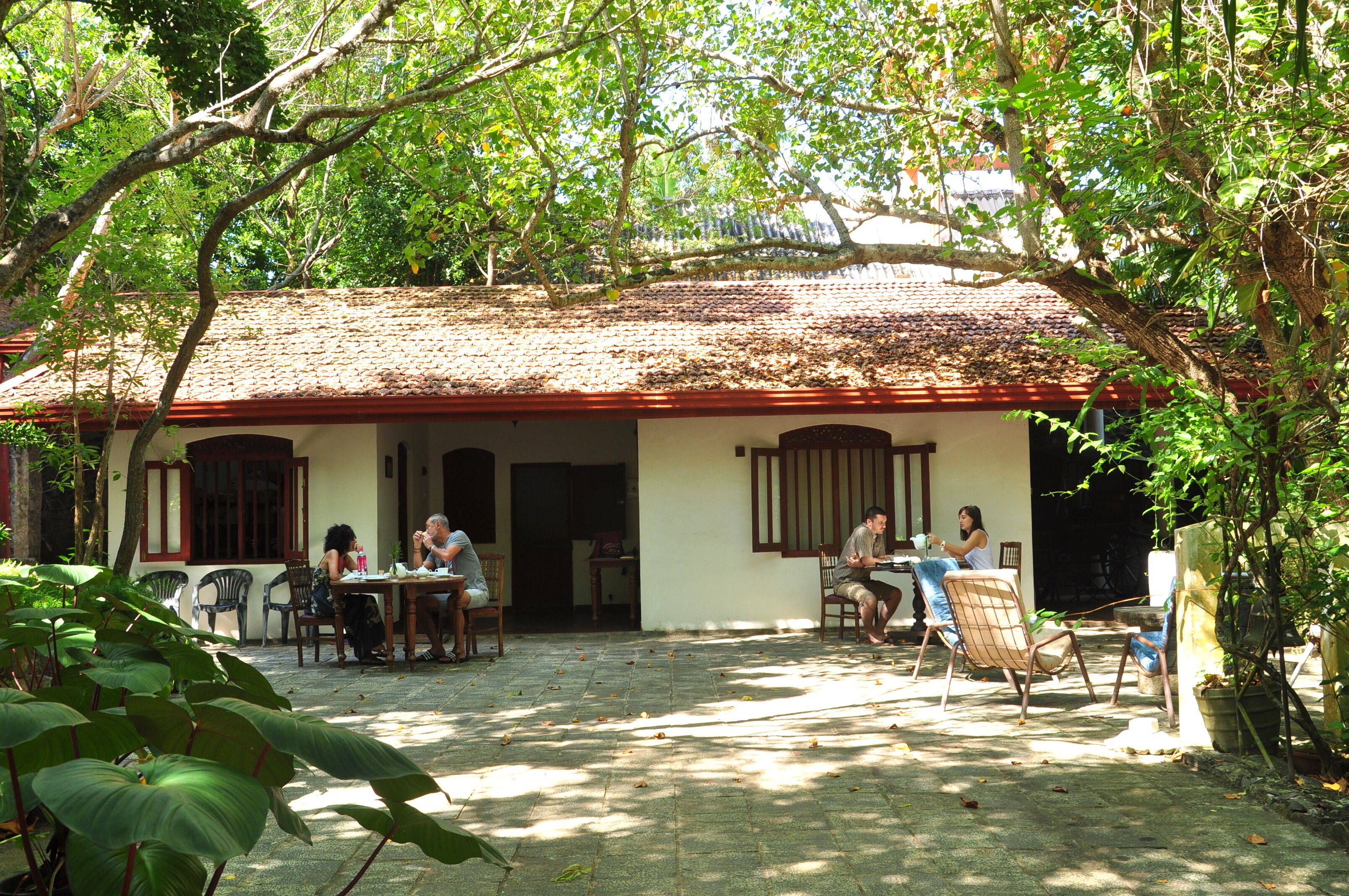 Ein traditionelles Haus mit Ziegeldach und einer Veranda. Mehrere Personen sitzen draußen an Tischen.