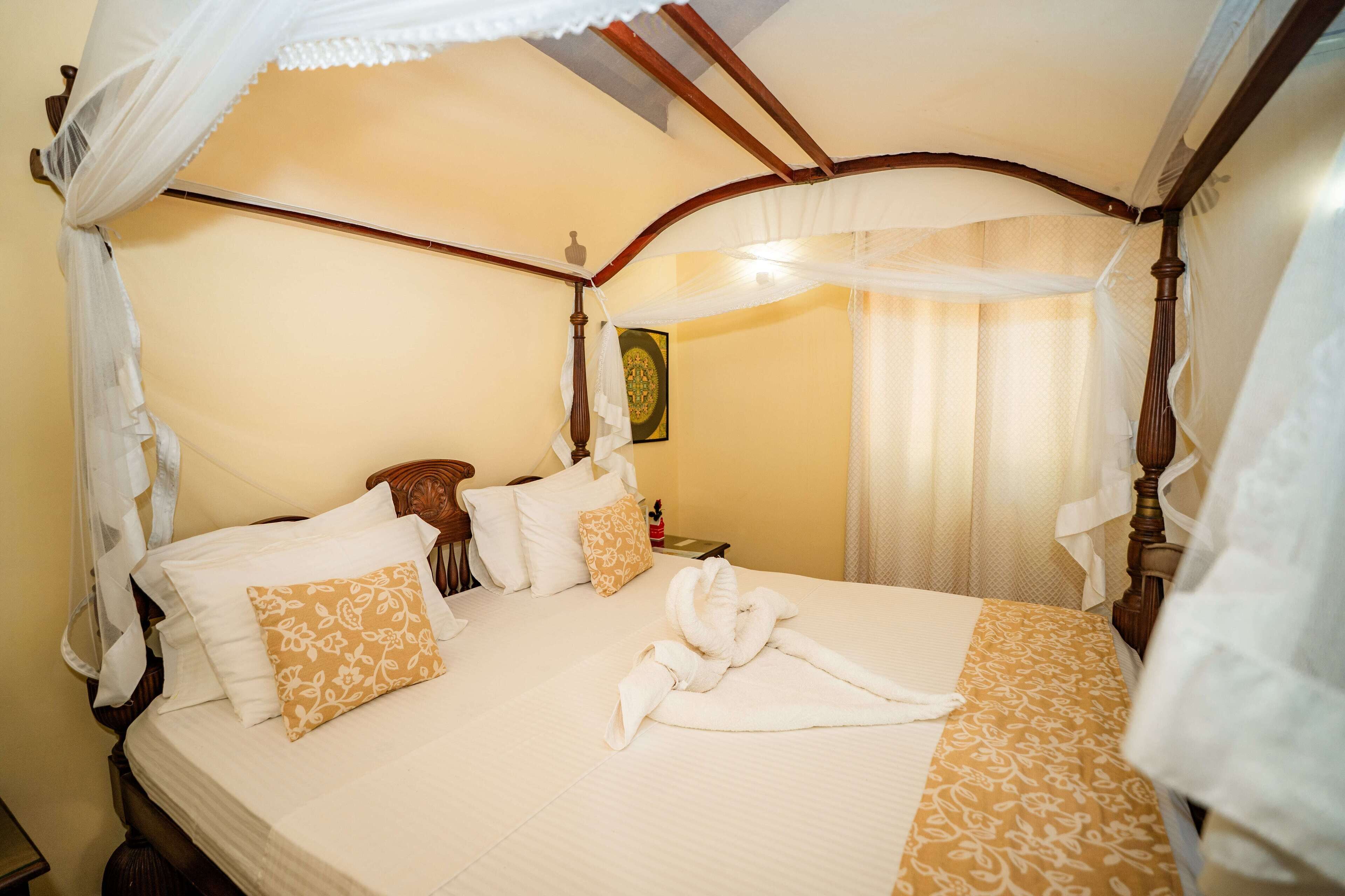 A four-poster bed with a canopy, multiple pillows, and a neatly folded towel on the bed.