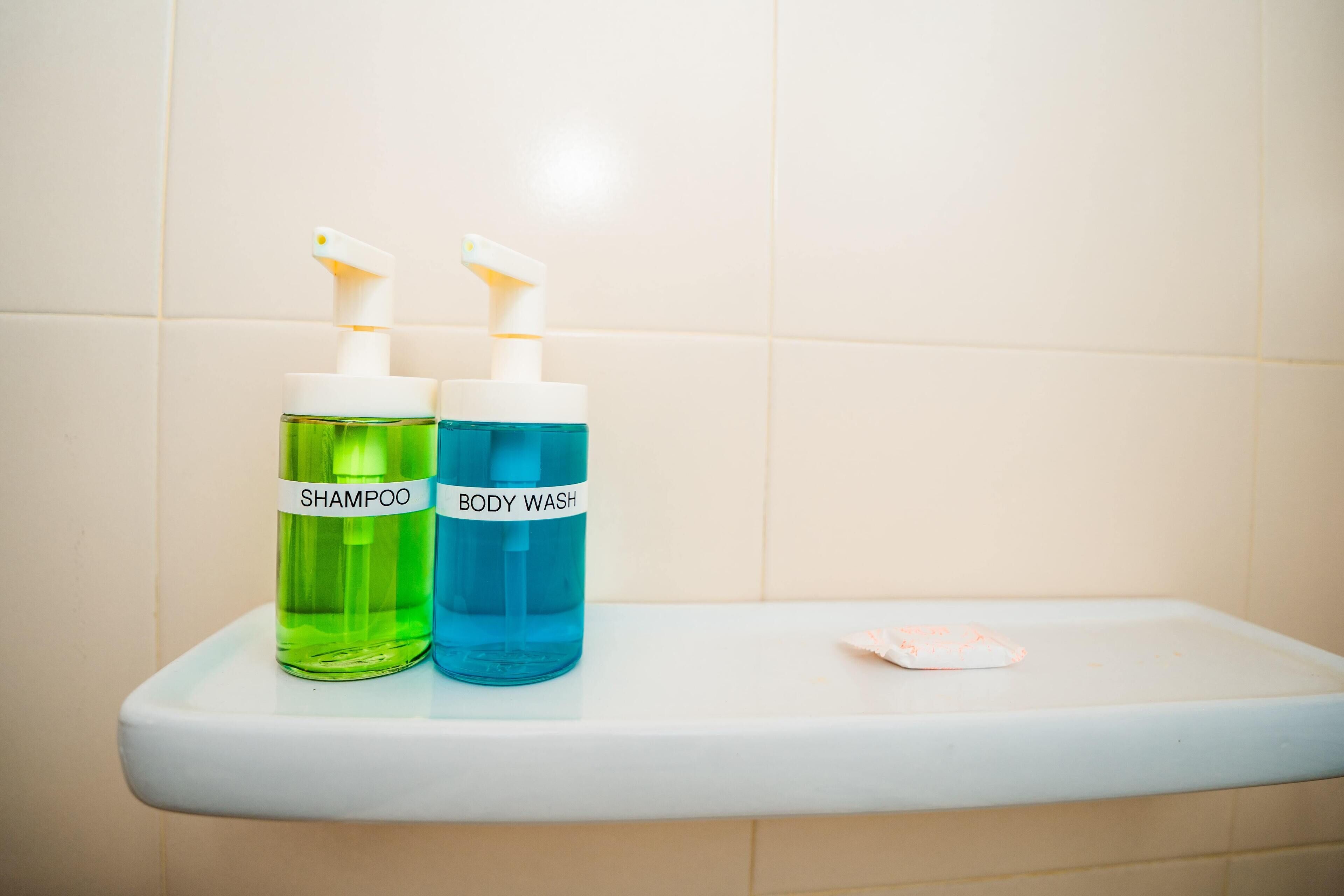 Two bottles of shampoo and body wash on a bathroom shelf.