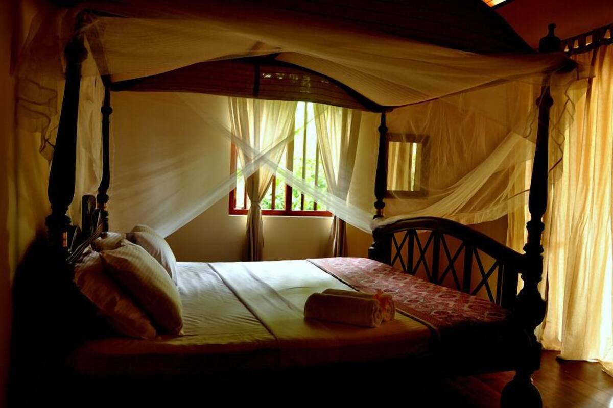 Una cama con dosel, una ventana con cortinas y un cabecero de madera.
