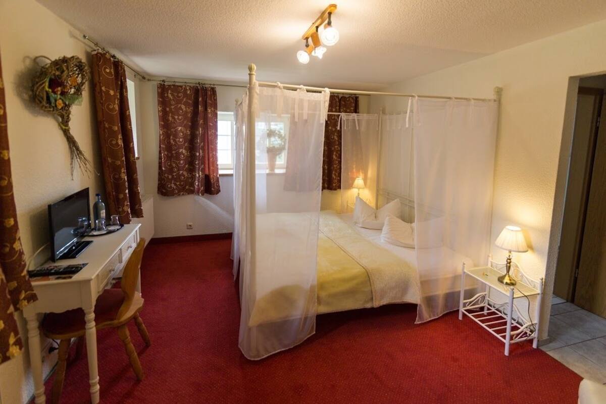 Un lit à baldaquin, un bureau avec un ordinateur et une table de chevet avec une lampe.