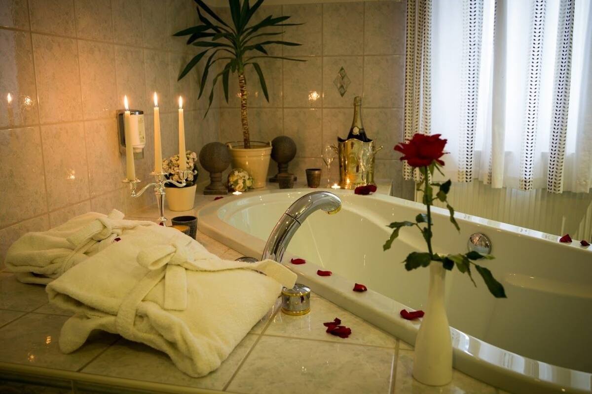 Une salle de bain luxueuse avec une grande baignoire, des serviettes blanches, un vase avec une rose et des objets décoratifs tels que des bougies et une plante.