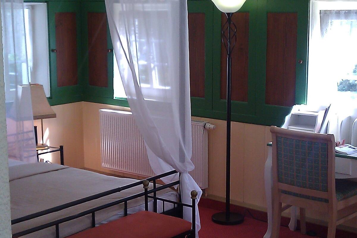 Une chambre à coucher avec un lit à baldaquin, une table de chevet, une chaise, une lampe et un radiateur.