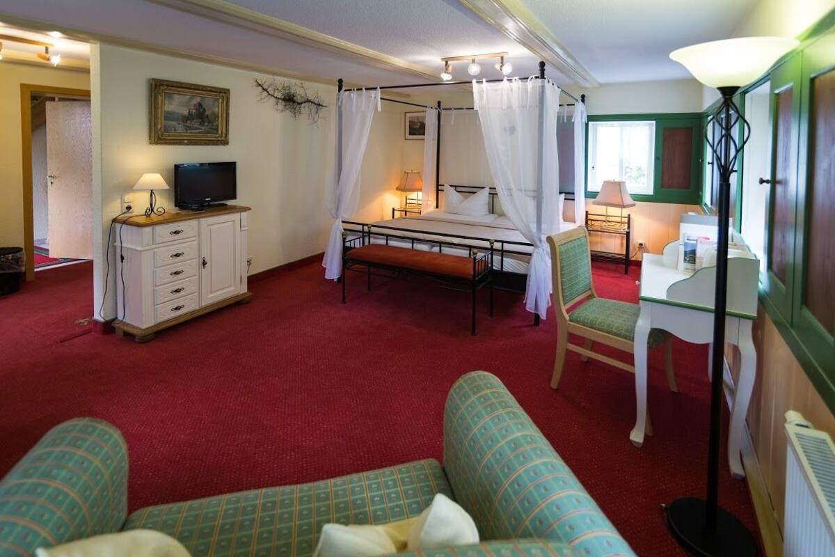 Une chambre avec un lit à baldaquin, un téléviseur posé sur un meuble, un bureau avec une lampe et un canapé.