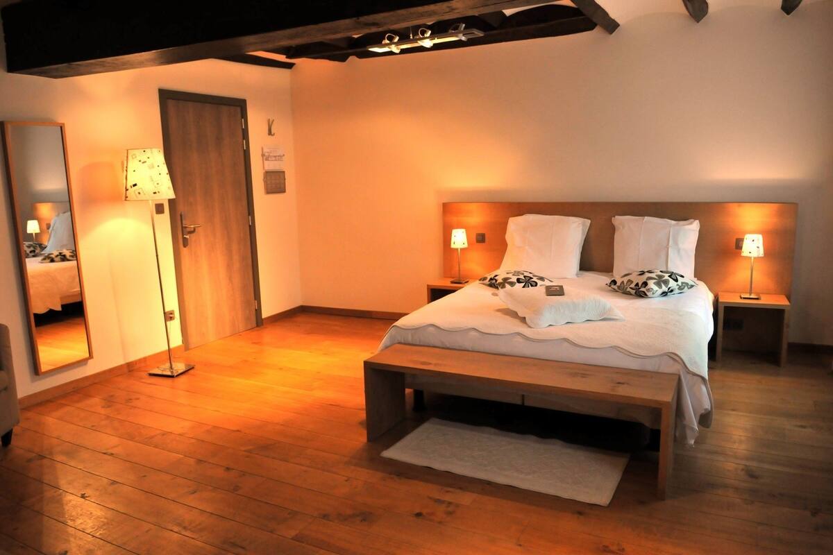 A bedroom with a wooden bed, two bedside tables with lamps, a mirror, and a wooden floor.