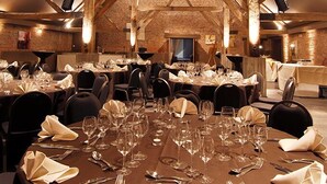 A spacious dining hall with high wooden beams and brick walls, featuring multiple round tables set for dining. - Hotel Le Val Fayt (Manage)