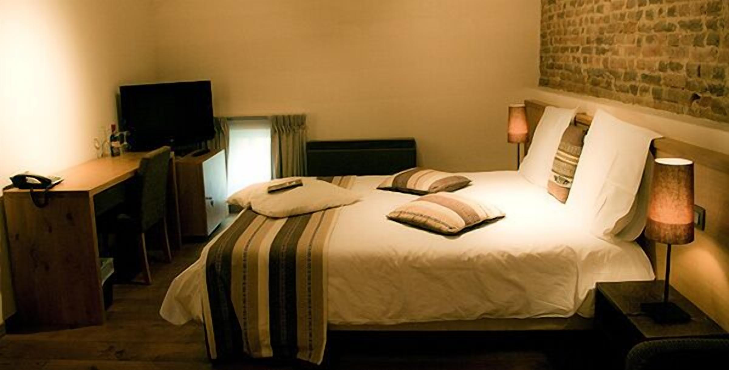 A hotel room with a bed, a desk, a television, and a lamp.