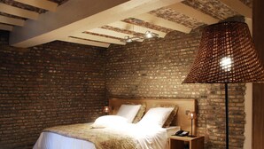 A bedroom with a brick wall, a wooden bed, a nightstand, and a floor lamp. - Hotel Le Val Fayt (Manage)