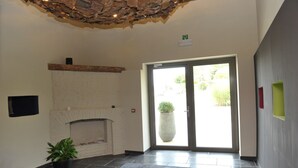 A hotel lobby with a fireplace, a reception desk, and a large glass door leading outside. - Hotel Le Val Fayt (Manage)