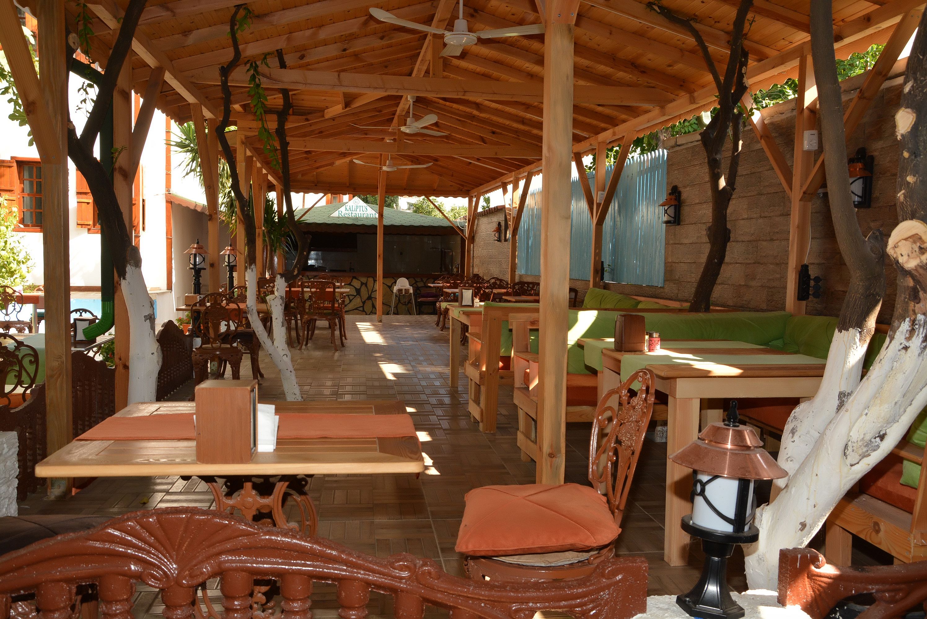 Un espace de restauration extérieur en bois, avec des tables et des chaises, un mur en pierre et un restaurant en arrière-plan.