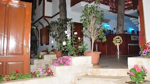 Zona de recepción con una escalera de madera, plantas en macetas y un cartel de recepción.