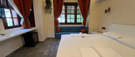 Una habitación de hotel con una cama grande, una ventana con cortinas, un sofá y un equipo de aire acondicionado.