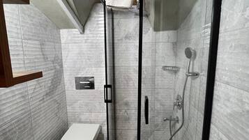 A modern bathroom with a glass-enclosed shower, a toilet, and a sink.