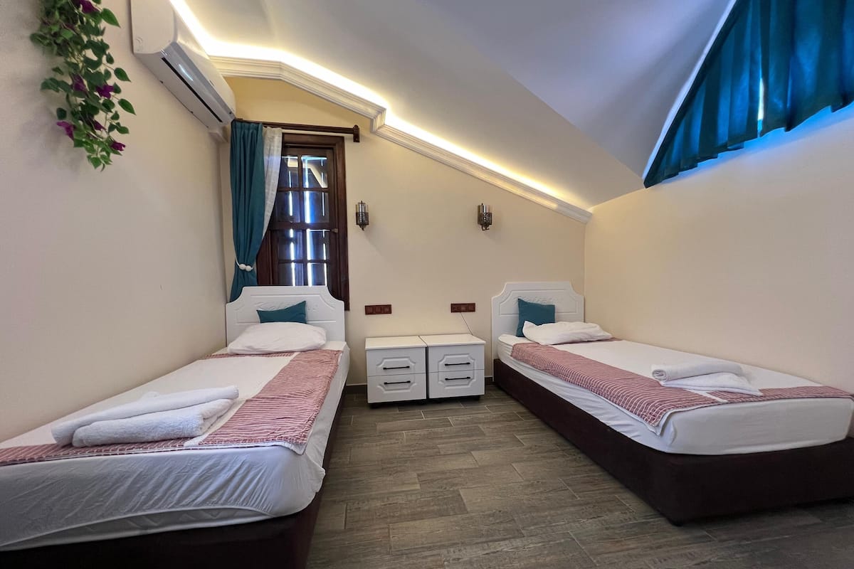 Ein Schlafzimmer mit zwei Einzelbetten, einem kleinen Nachttisch mit Schubladen, einer Wand-Klimaanlage und einem Fenster mit Vorhängen.