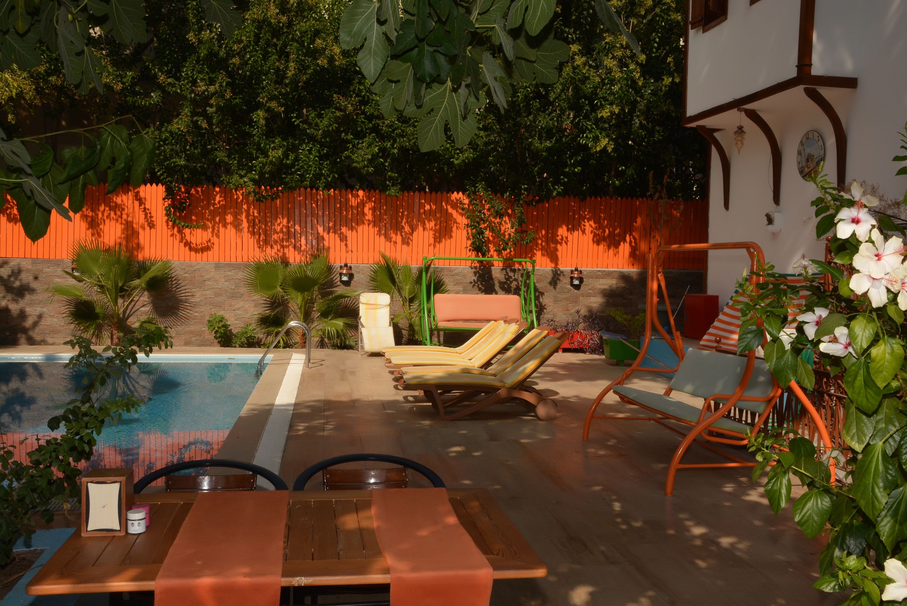 Un área junto a la piscina con mesa de madera, sillones de descanso y una silla colgante.