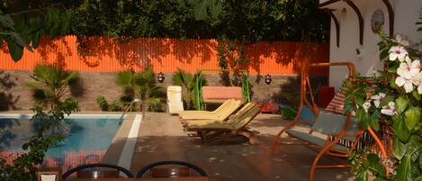 Un área junto a la piscina con mesa de madera, sillones de descanso y una silla colgante.