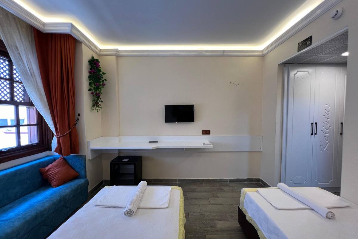 Ein Hotelzimmer mit einer Couch, zwei Betten, einem Fernseher, einem kleinen Tisch und einem Kleiderschrank.