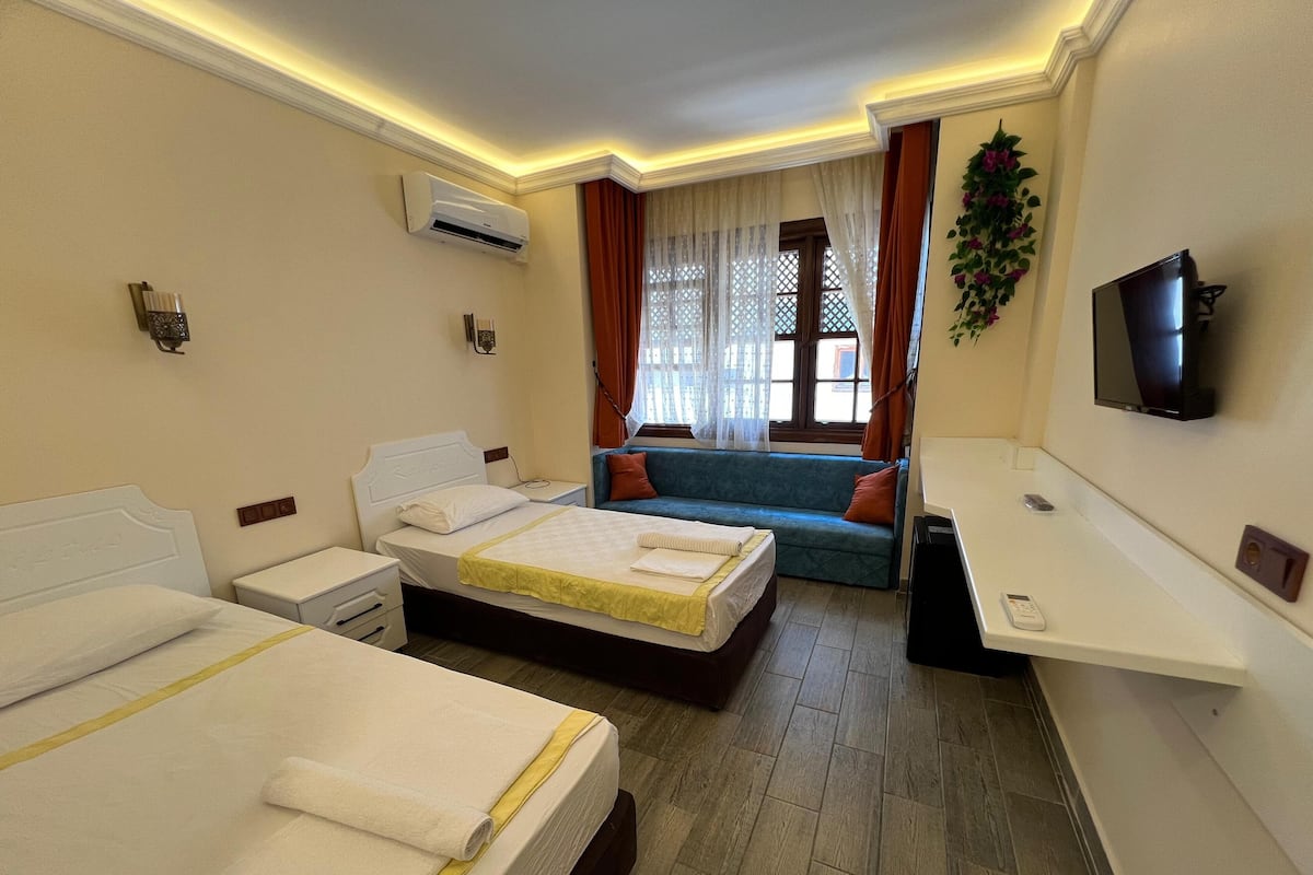 Ein Hotelzimmer mit zwei Betten, einem Sofa, einem Fernseher und einer Klimaanlage.