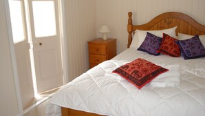 A bedroom with a wooden bed, white bedding, and a nightstand with a lamp. - Twisted Gum Cottage (Ballandean)