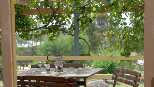An outdoor wooden deck with a table and chairs, surrounded by greenery. - Twisted Gum Cottage (Ballandean)