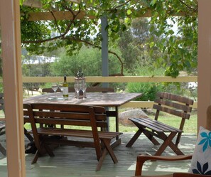 An outdoor wooden deck with a table and chairs, surrounded by greenery. - Twisted Gum Cottage (Ballandean)
