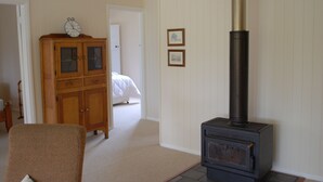 A room with a wooden cabinet, a bed, and a black wood-burning stove. - Twisted Gum Cottage (Ballandean)