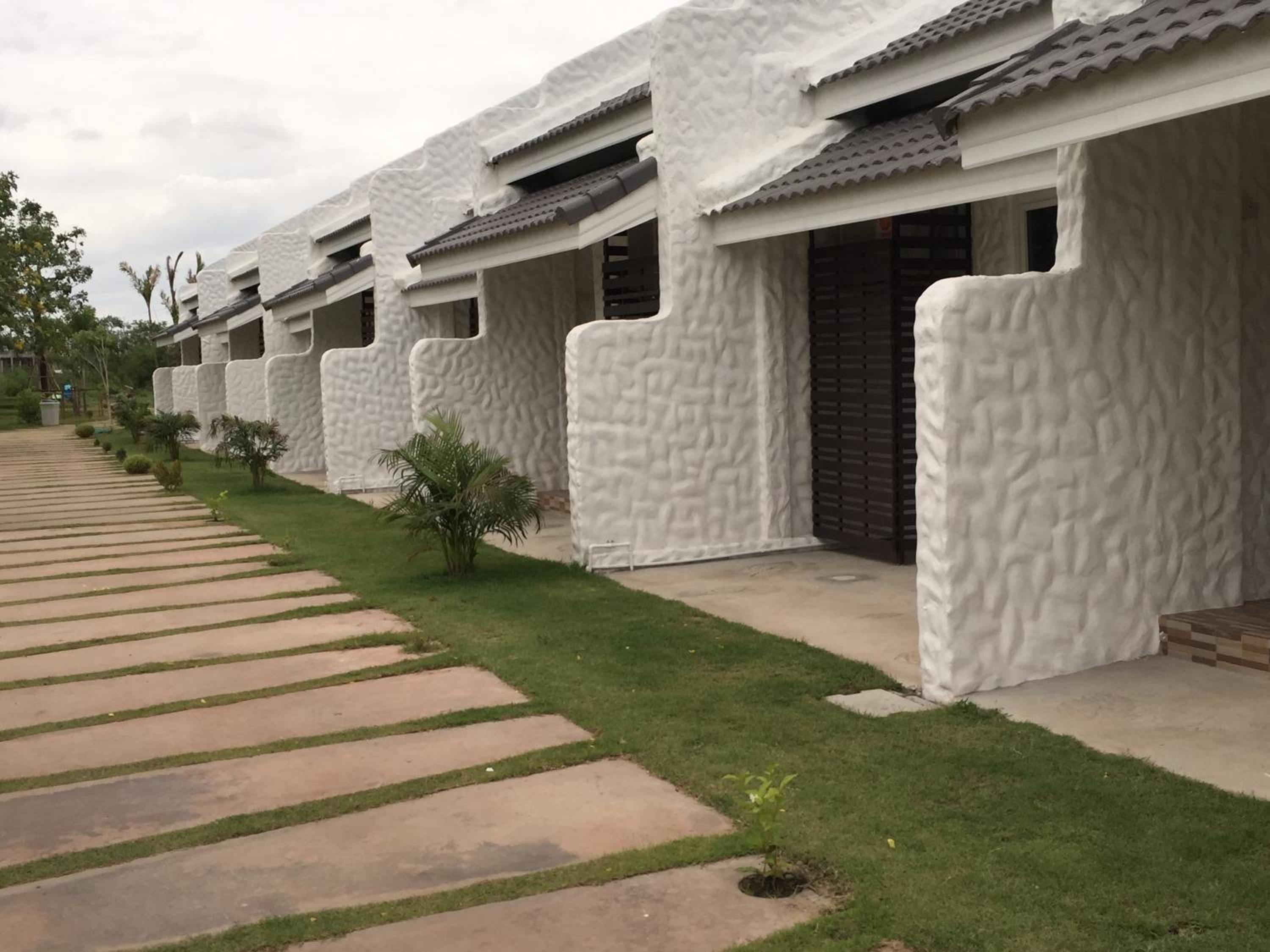 A row of modern buildings with textured white walls and dark roofs, arranged in a linear fashion along a paved walkway.
