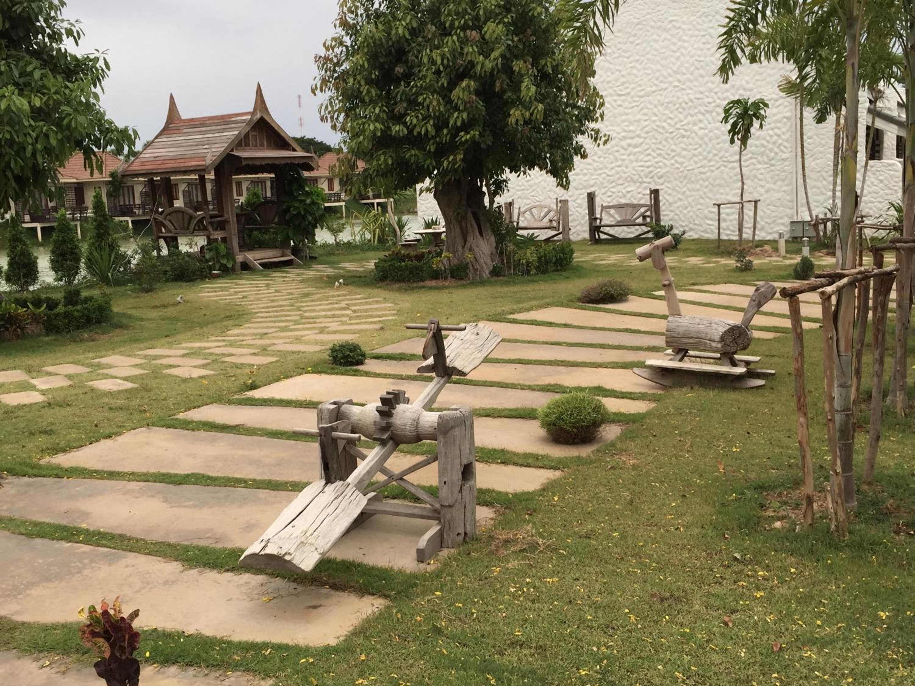 Un jardín con un conjunto de columpios de madera, un pabellón y un estanque.