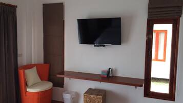 A room with a flat-screen TV mounted on the wall, a red chair, a small wooden stool, and a window with a view of greenery.
