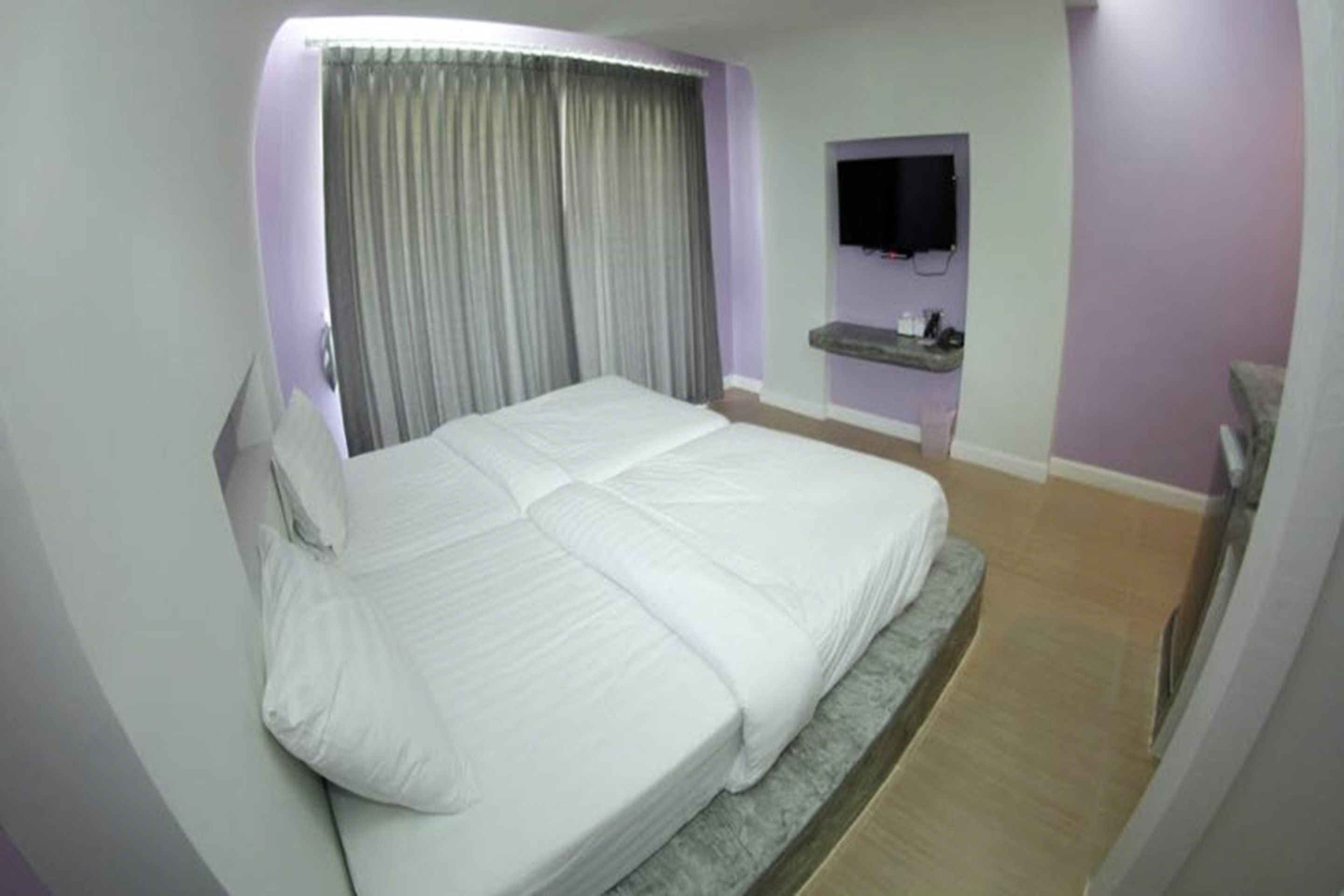 A hotel room with a large bed, a TV mounted on the wall, and a small shelf with toiletries.