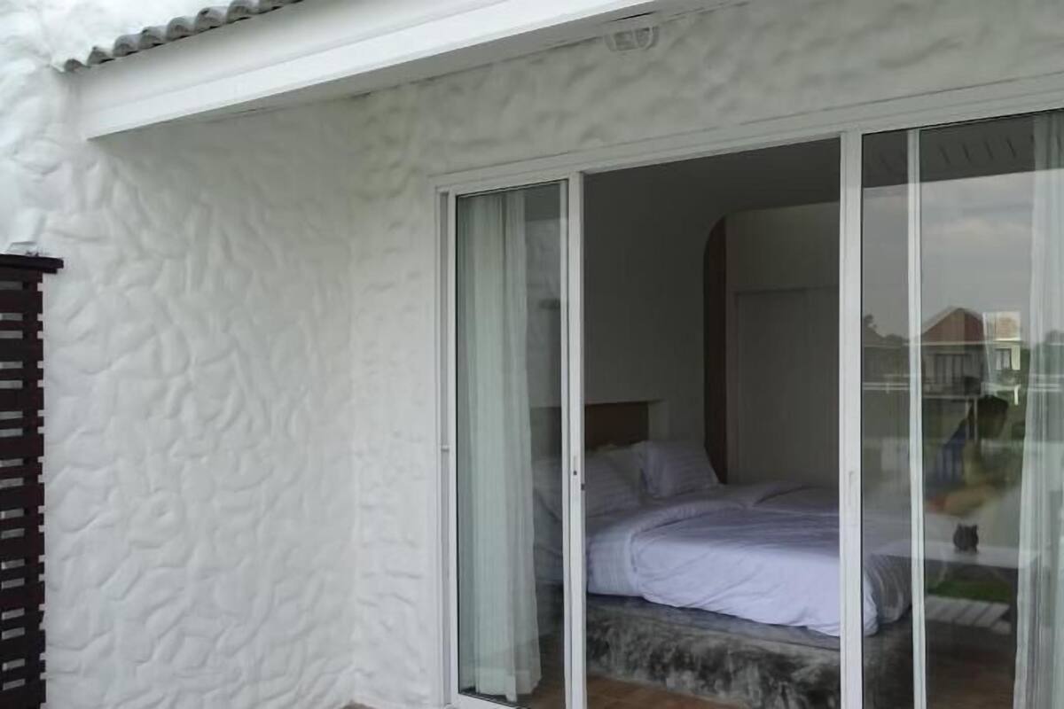 A bedroom with a bed, a sliding glass door, and a view of the outside.