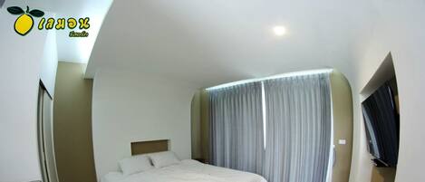 A modern hotel room with a bed, a small seating area, a television, and a window with curtains.